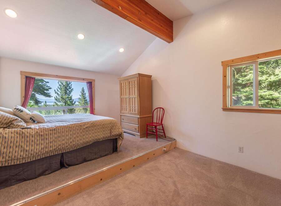 Experience breathtaking views from this elevated bedroom, featuring a spacious bed with a patterned comforter and a large window overlooking a serene landscape.