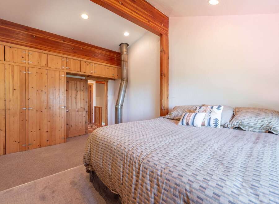 Experience rustic charm in this cozy bedroom featuring a large wooden wardrobe and a comfortable bed adorned with decorative pillows.