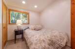This cozy bedroom features a comfortable bed with a floral comforter, a bedside table with a lamp, and a window offering serene forest views.