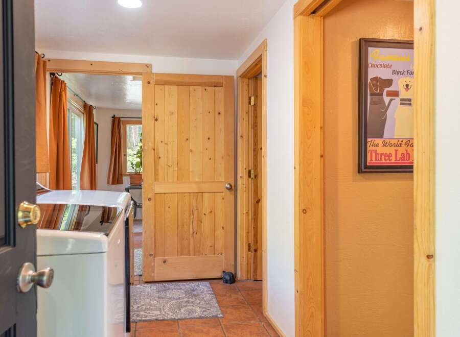 Discover a charming interior featuring a laundry area with a washing machine, complemented by warm orange curtains and natural wood accents throughout.