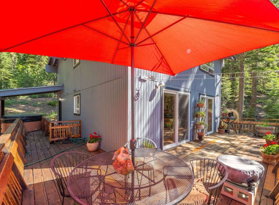 Enjoy outdoor living on this spacious wooden deck, complete with a large red umbrella for shade and a dining set for al fresco meals.