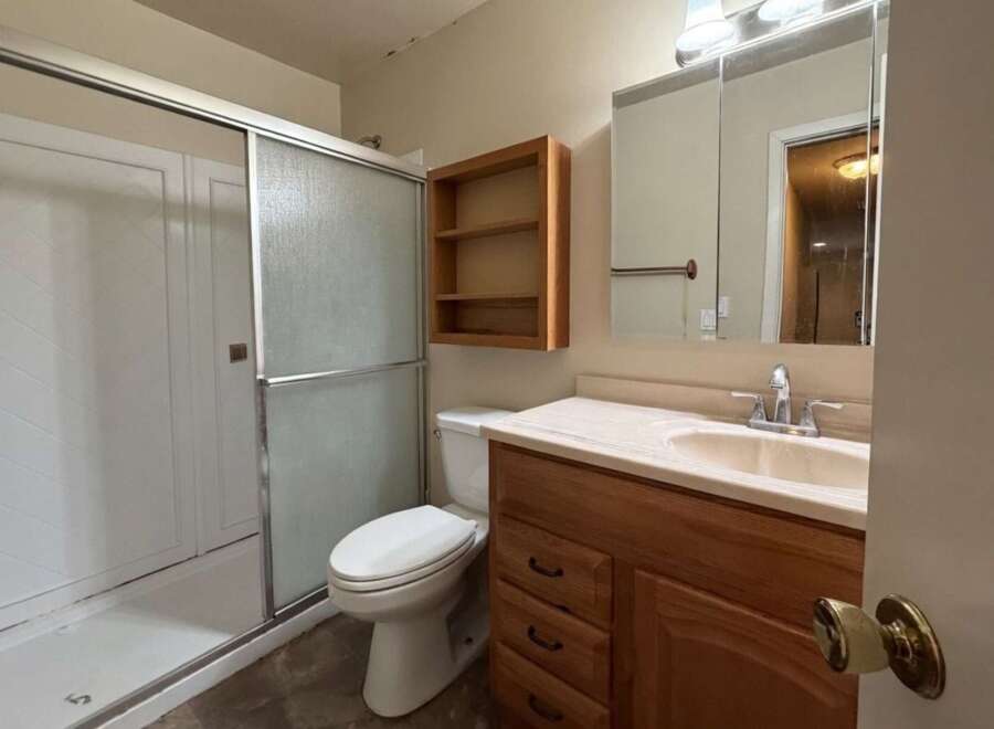 This bathroom features a spacious shower with sliding glass doors, a comfortable toilet, and a wooden vanity with a sink and ample storage.