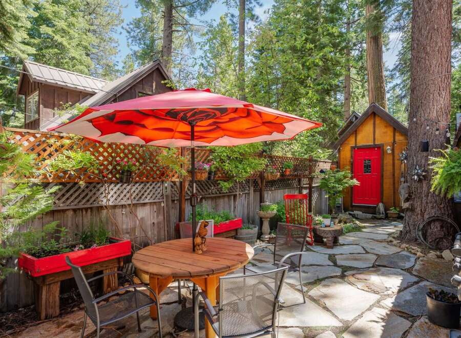 Enjoy outdoor living in this charming backyard oasis, complete with a stone patio and a vibrant red umbrella providing shade over a wooden dining set.