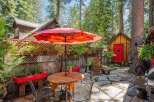 Enjoy outdoor living in this charming backyard oasis, complete with a stone patio and a vibrant red umbrella providing shade over a wooden dining set.