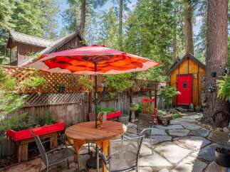 Enjoy outdoor living in this charming backyard oasis, complete with a stone patio and a vibrant red umbrella providing shade over a wooden dining set.