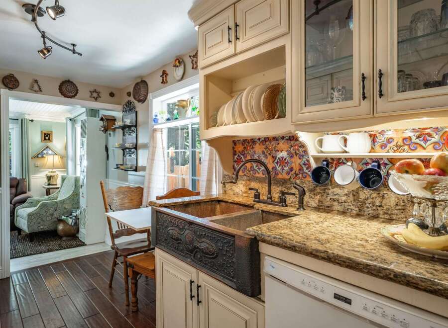 This charming kitchen boasts a stunning copper farmhouse sink with intricate detailing, complemented by a vibrant, colorful backsplash.
