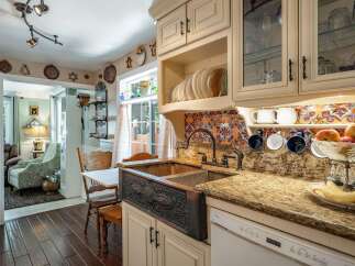 This charming kitchen boasts a stunning copper farmhouse sink with intricate detailing, complemented by a vibrant, colorful backsplash.