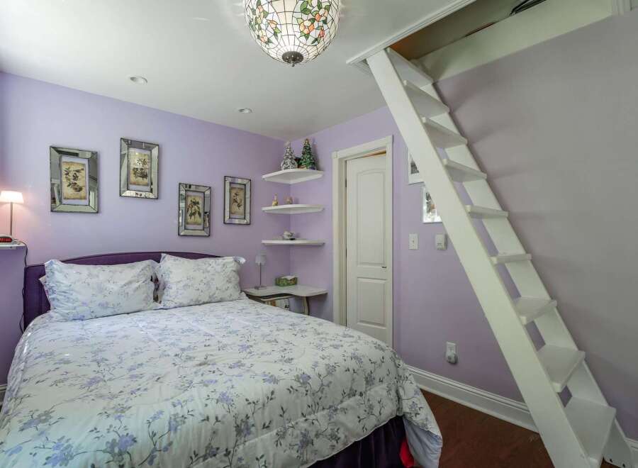Discover this charming bedroom featuring a comfortable queen-size bed with a floral comforter and a stylish purple headboard.