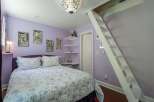 Discover this charming bedroom featuring a comfortable queen-size bed with a floral comforter and a stylish purple headboard.