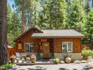 Charming wooden cabin nestled amongst tall pine trees, featuring a welcoming porch adorned with potted flowers and a rustic.
