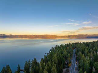 Experience breathtaking lakefront living with this stunning aerial view of a property nestled amidst a lush pine forest.