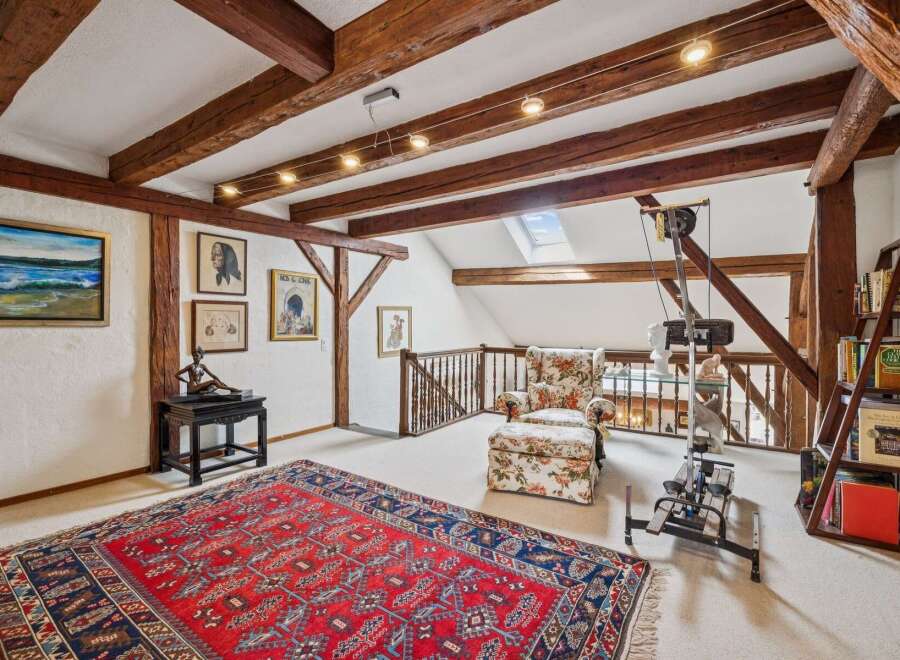 This charming attic space boasts exposed wooden beams and a cozy reading nook with a floral armchair and ottoman.