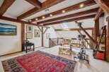 This charming attic space boasts exposed wooden beams and a cozy reading nook with a floral armchair and ottoman.