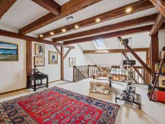 This charming attic space boasts exposed wooden beams and a cozy reading nook with a floral armchair and ottoman.