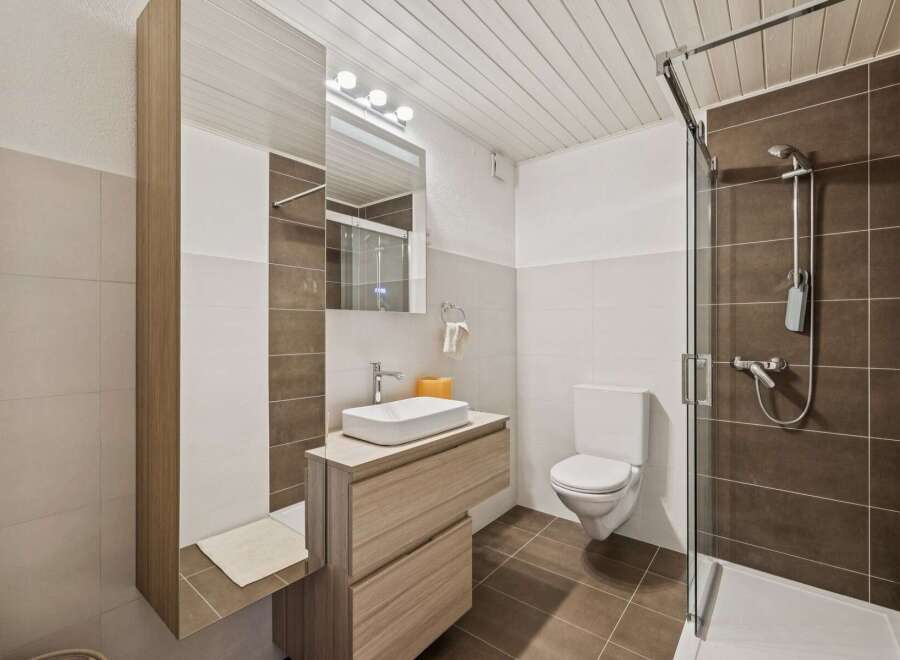 This modern bathroom features a sleek vanity with a vessel sink and ample storage, complemented by a large mirror and bright vanity lighting.