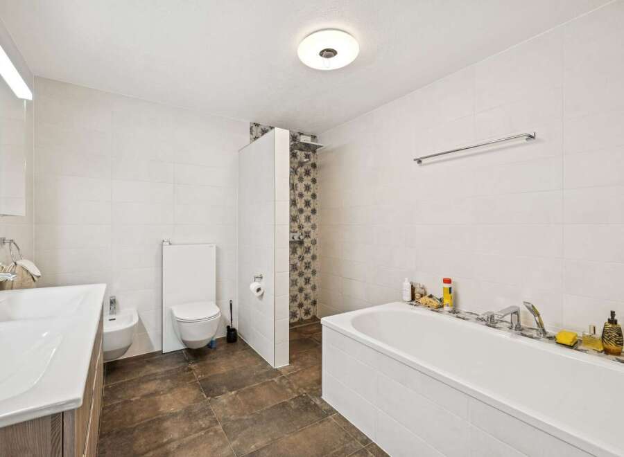 This spacious bathroom features a modern white bathtub, a separate shower area with decorative tile accents, and a sleek vanity with a large sink.