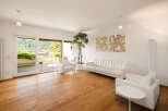 Experience modern living in this spacious apartment featuring a bright and airy living room with sleek white furniture and a large plant.