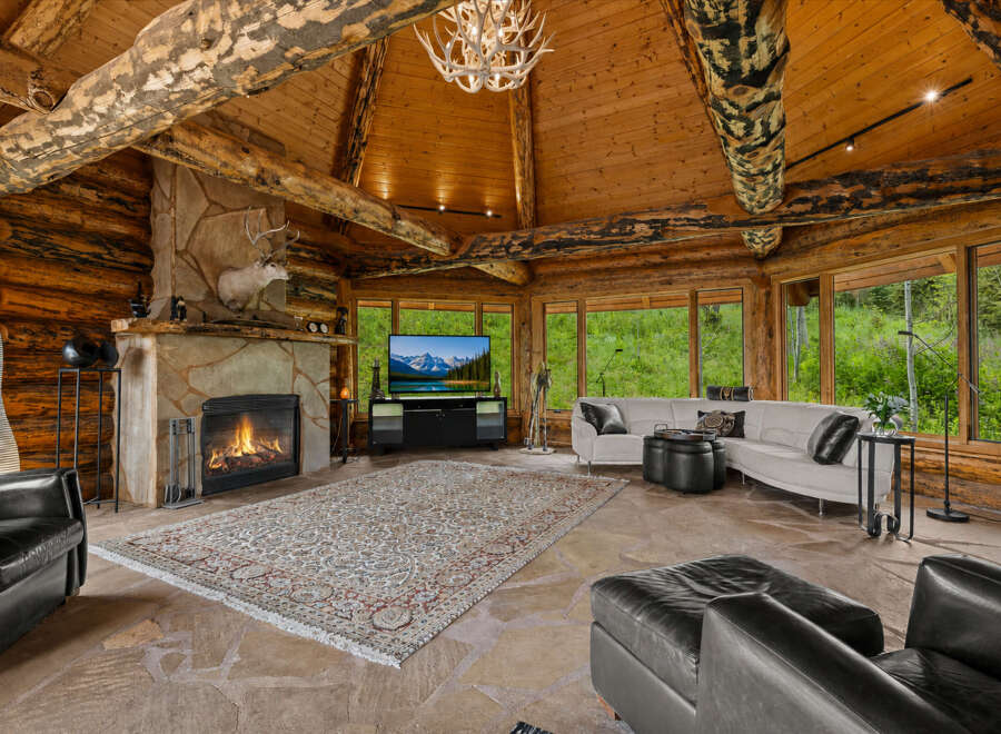 Experience rustic luxury in this stunning log cabin living room, featuring a grand stone fireplace with a mounted deer head and a cozy seating area.