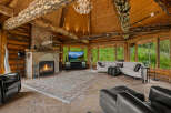 Experience rustic luxury in this stunning log cabin living room, featuring a grand stone fireplace with a mounted deer head and a cozy seating area.