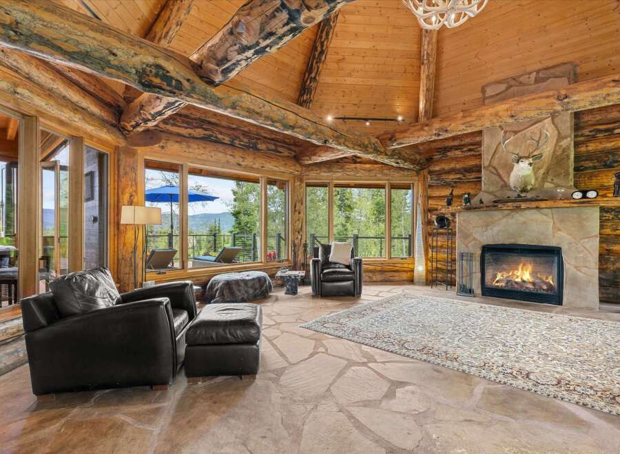 Experience rustic luxury in this stunning log cabin living room, featuring a grand stone fireplace and expansive windows with breathtaking mountain views.