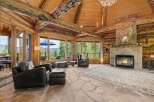 Experience rustic luxury in this stunning log cabin living room, featuring a grand stone fireplace and expansive windows with breathtaking mountain views.