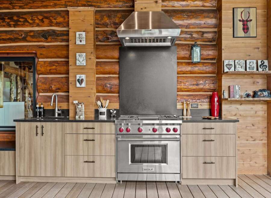 Experience rustic charm in this log cabin kitchen, featuring a professional Wolf range and a sleek stainless steel hood.