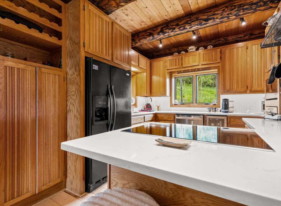 Experience rustic charm in this spacious kitchen featuring warm wood cabinetry and a stunning log beam ceiling.