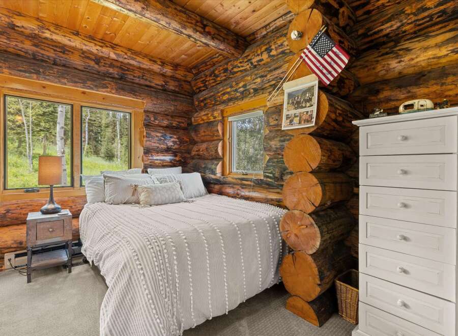 Experience rustic charm in this cozy log cabin bedroom, featuring a comfortable bed adorned with plush pillows and a textured duvet.