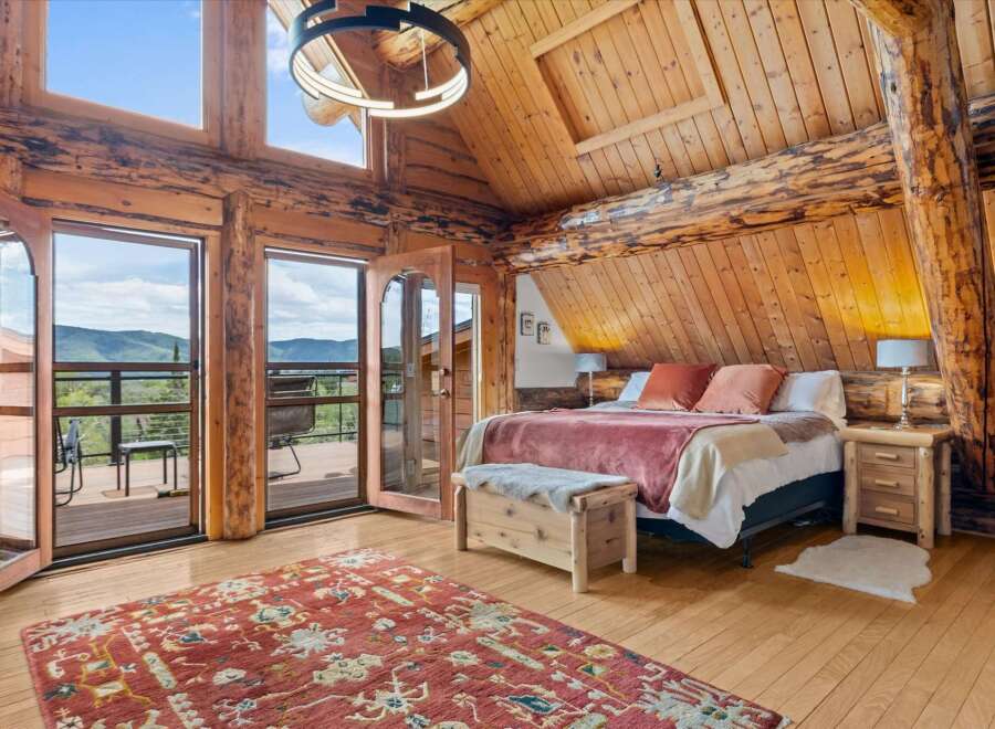 Experience rustic luxury in this stunning log cabin bedroom, featuring expansive windows with breathtaking mountain views.
