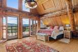 Experience rustic luxury in this stunning log cabin bedroom, featuring expansive windows with breathtaking mountain views.