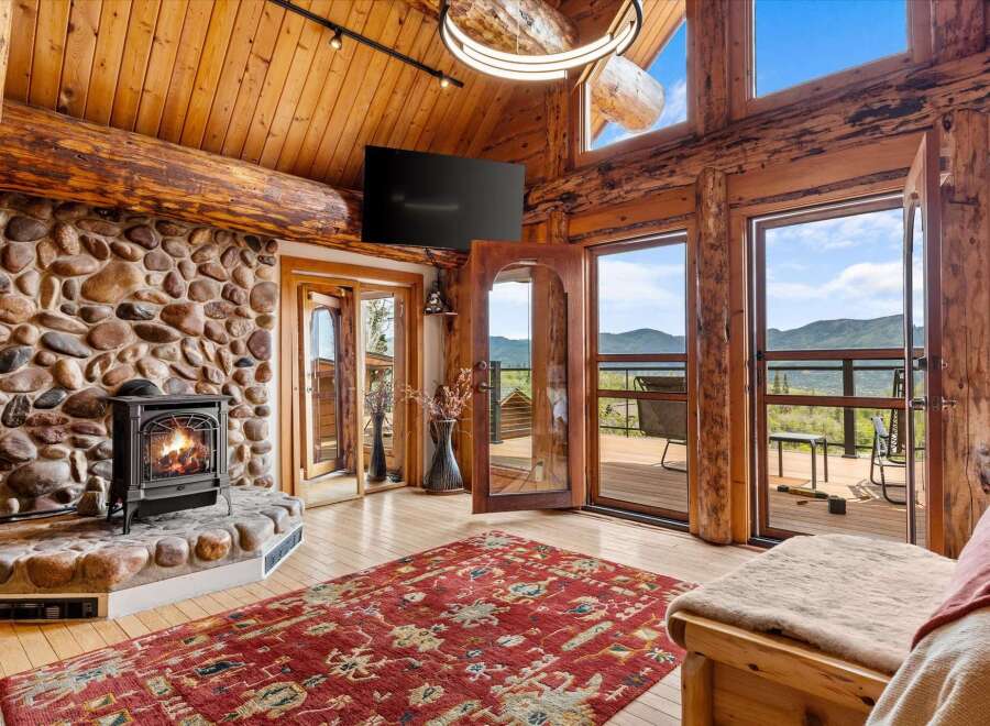 Experience rustic luxury in this stunning log cabin living room, featuring a grand stone fireplace and exposed wooden beams.