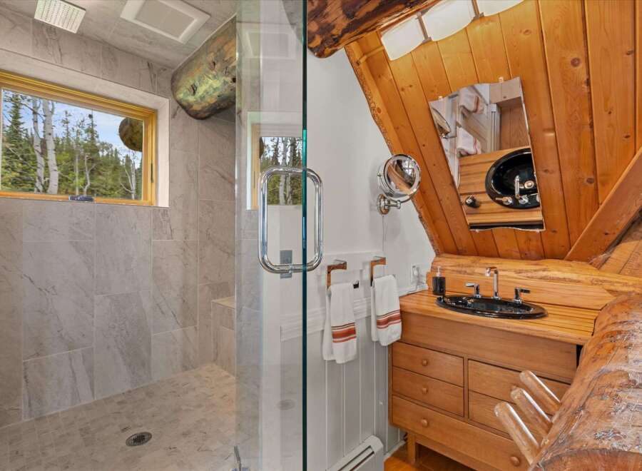 Experience rustic charm in this unique bathroom featuring a spacious walk-in shower with elegant tile work and a scenic window overlooking a forest.