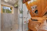Experience rustic charm in this unique bathroom featuring a spacious walk-in shower with elegant tile work and a scenic window overlooking a forest.