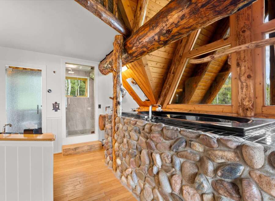 Experience rustic luxury in this unique bathroom featuring a stunning stone-clad vanity and a deep soaking tub.