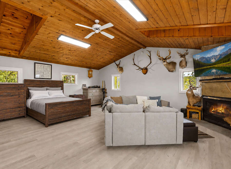 Experience rustic charm in this unique bedroom and living space, featuring a cozy wooden ceiling, a comfortable bed, and a fireplace with a mounted TV.