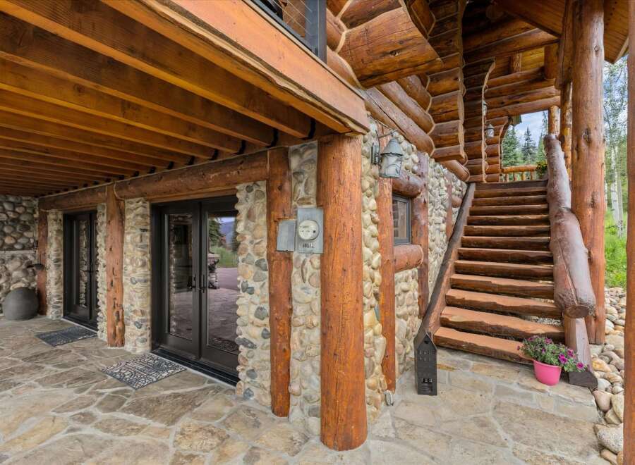Experience rustic charm with this stunning log home featuring a stone foundation and a grand wooden staircase leading to the upper level.