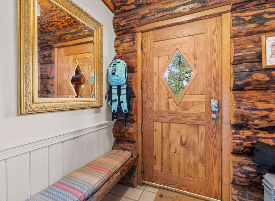 Step into a charming log cabin entryway featuring a rustic wooden door with a diamond-shaped window, perfect for letting in natural light.