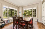 Enjoy meals with a view in this charming dining room, featuring a large wooden table and chairs set against a backdrop of lush greenery through expansive windows.