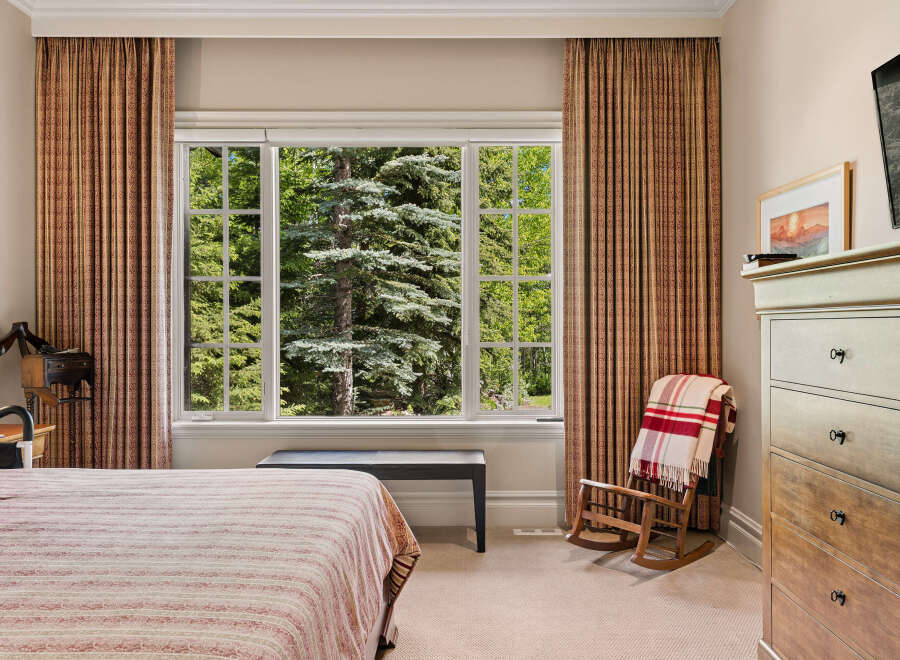 Experience serene living with this charming bedroom featuring a large window that offers breathtaking views of lush greenery and mature trees.