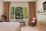 Experience serene living with this charming bedroom featuring a large window that offers breathtaking views of lush greenery and mature trees.