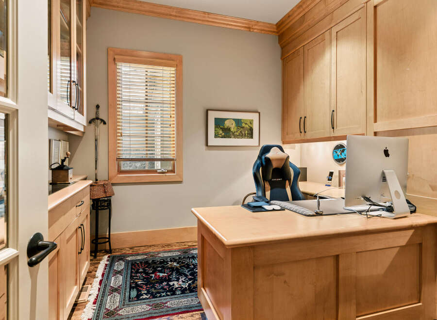 This home office features custom light wood cabinetry with glass-fronted upper cabinets, providing ample storage and display space.