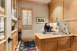 This home office features custom light wood cabinetry with glass-fronted upper cabinets, providing ample storage and display space.