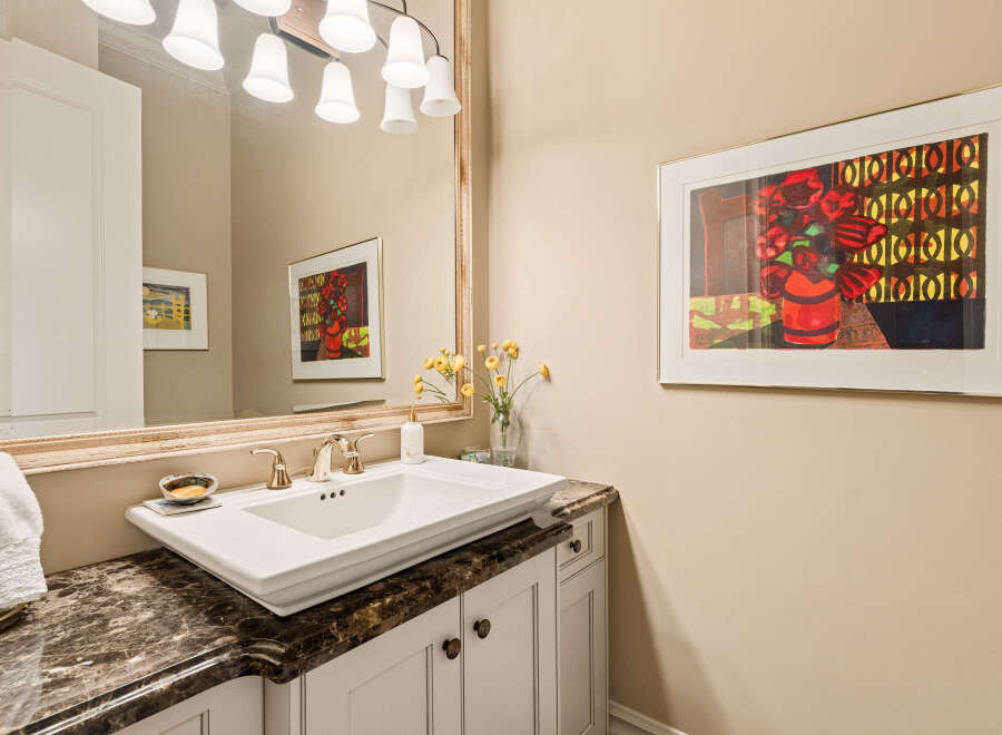 This elegant bathroom features a vessel sink atop a dark marble countertop, complemented by a decorative mirror and a vibrant floral artwork.