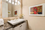 This elegant bathroom features a vessel sink atop a dark marble countertop, complemented by a decorative mirror and a vibrant floral artwork.