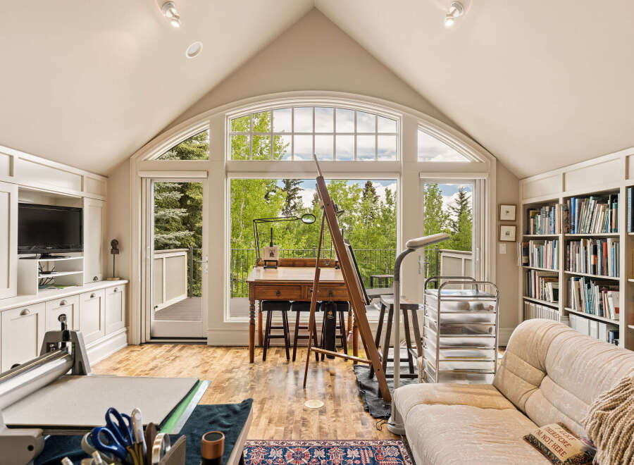 Discover an artist's dream studio bathed in natural light, featuring a large arched window with stunning forest views.