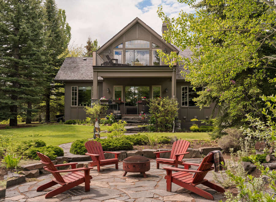 Enjoy the outdoors with this charming backyard featuring a stone patio, a fire pit, and comfortable Adirondack chairs perfect for gathering.