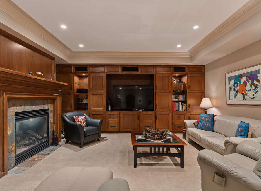 This inviting living room features a cozy fireplace with a stone surround, complemented by extensive custom wood cabinetry that houses a large television and offers ample storage.