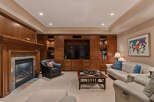 This inviting living room features a cozy fireplace with a stone surround, complemented by extensive custom wood cabinetry that houses a large television and offers ample storage.