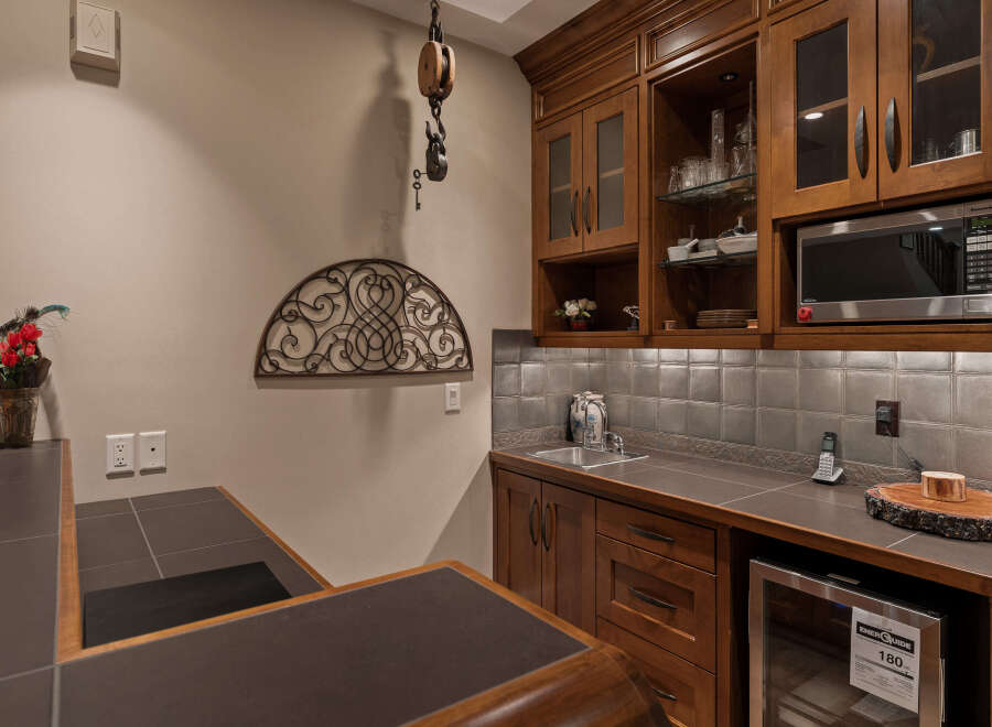 This custom bar area features rich wood cabinetry, a sleek stainless steel sink, and a microwave, perfect for entertaining.