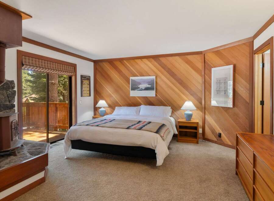 Experience cozy mountain living in this charming bedroom featuring a rustic stone fireplace and a sliding glass door leading to a private deck with forest views.